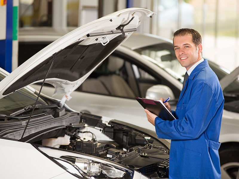Smiling technician servicing a car with notepad in hand